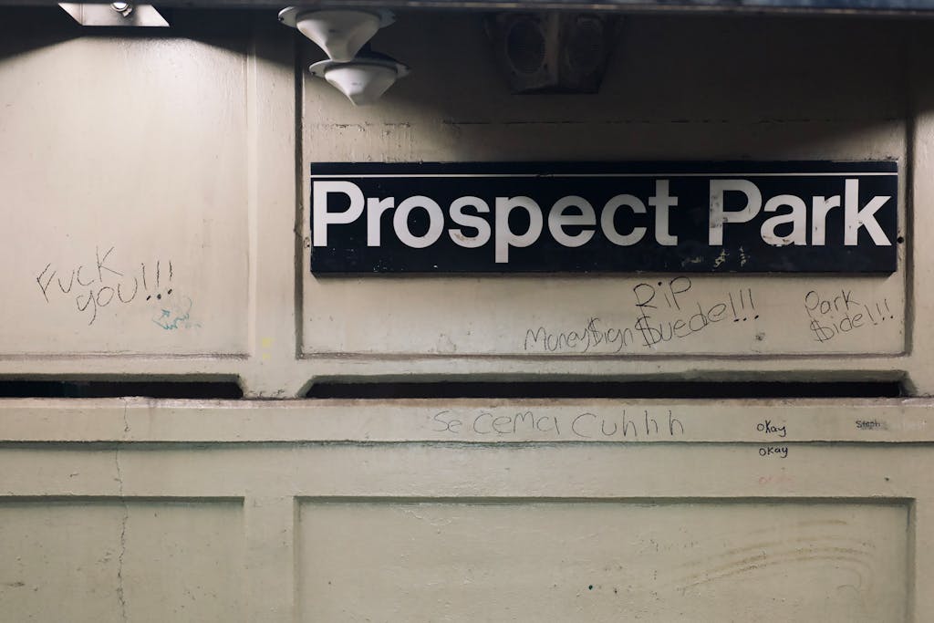 Graffiti-covered subway sign at Prospect Park station, showcasing urban street art.