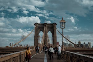 Khair Staffing People walking on Brooklyn Bridge with a view of the Manhattan skyline under a cloudy sky.