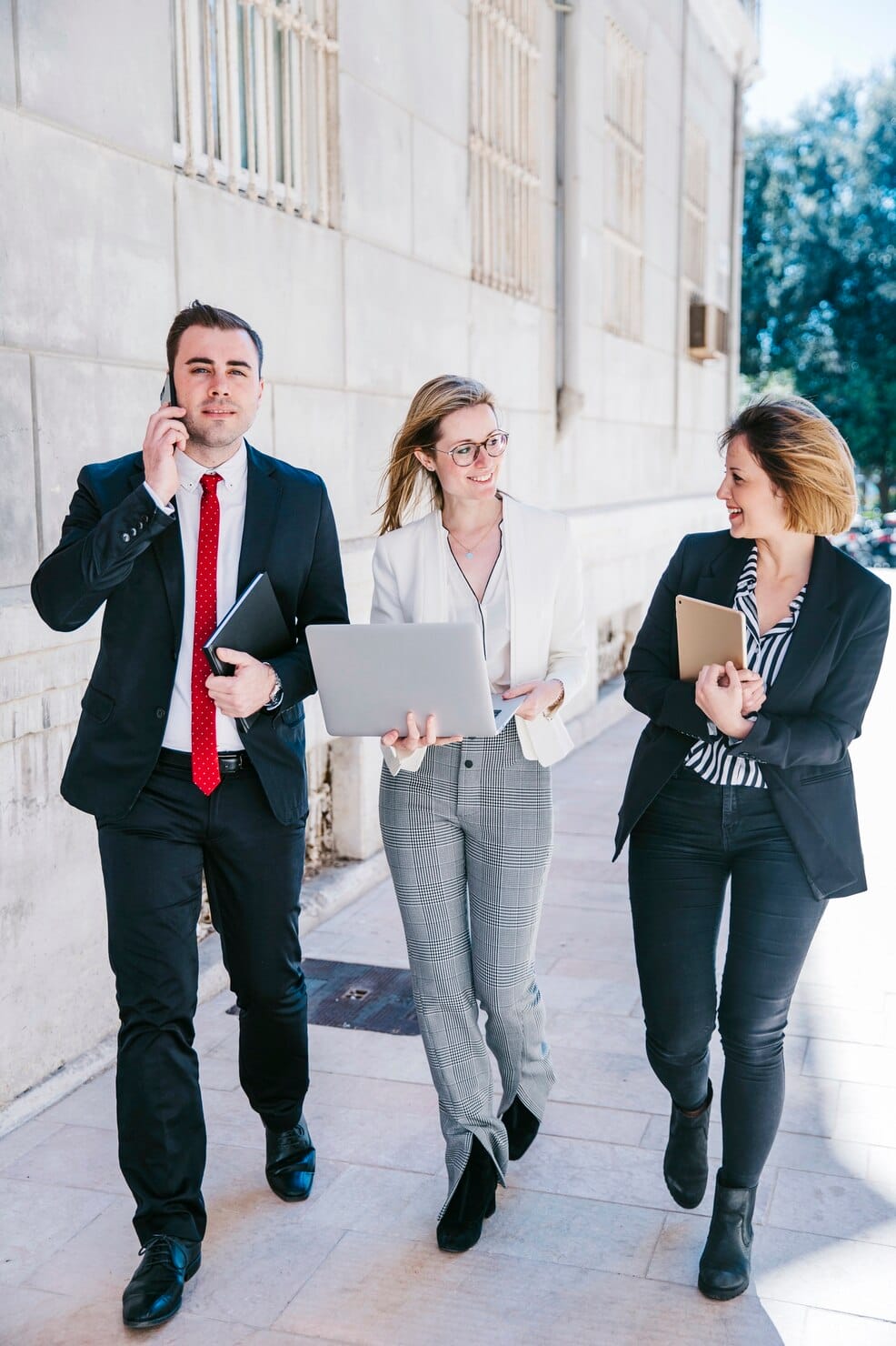 Business professionals discussing work while carrying a laptop and tablet